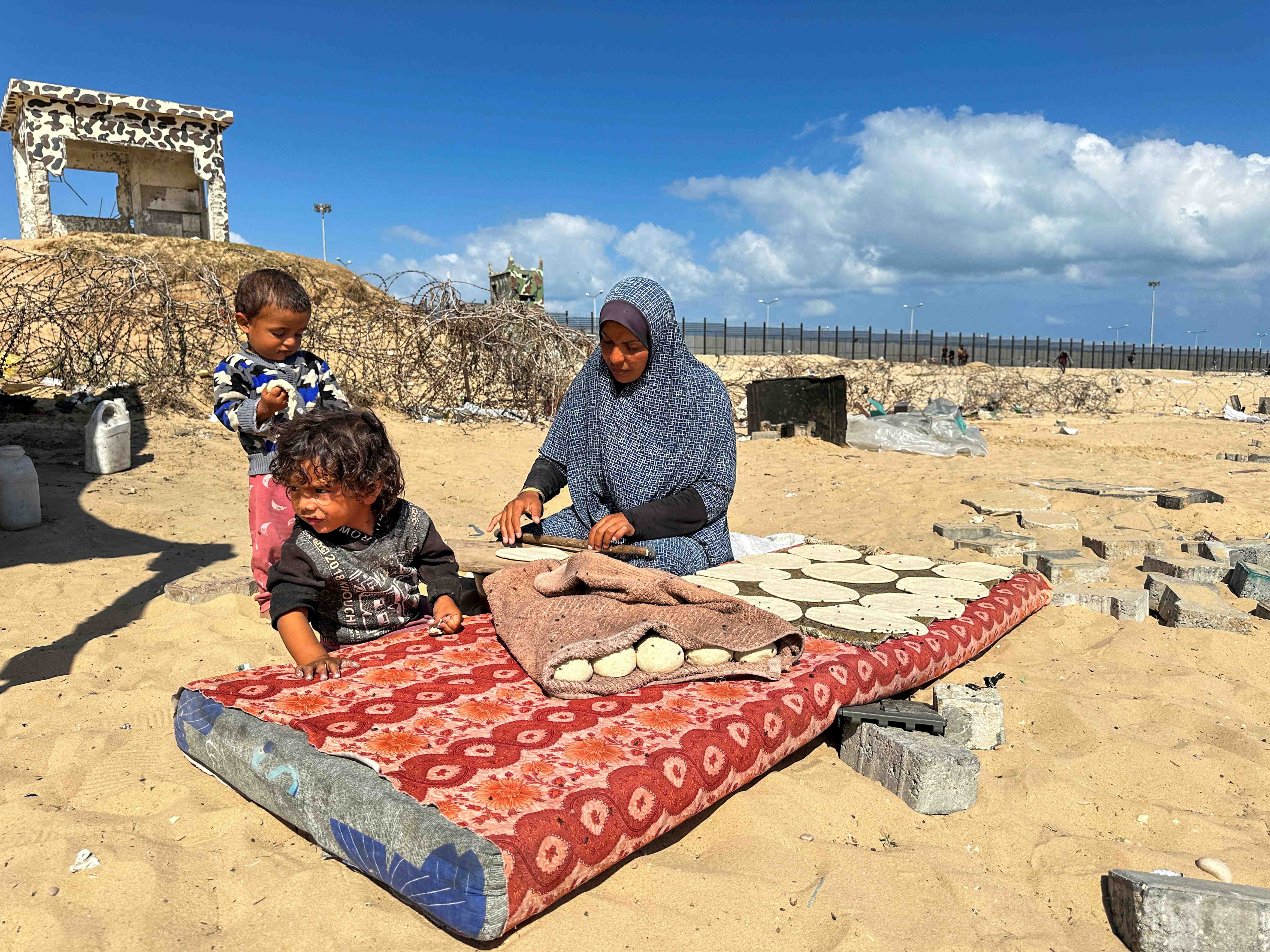 A woman prepares food next to children, as displaced Palestinians take shelter at the border with Egypt, during an Israeli military operation, in Rafah in the southern Gaza Strip. REUTERS