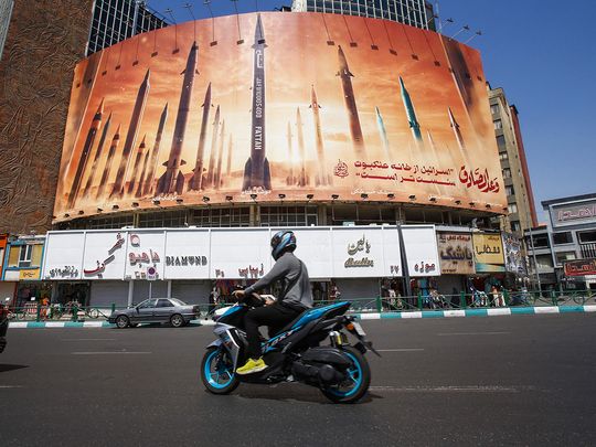 A man rides a motorbike past a billboard depicting Iranian ballistic missiles in service in Tehran on April 19, 2024. (AFP)